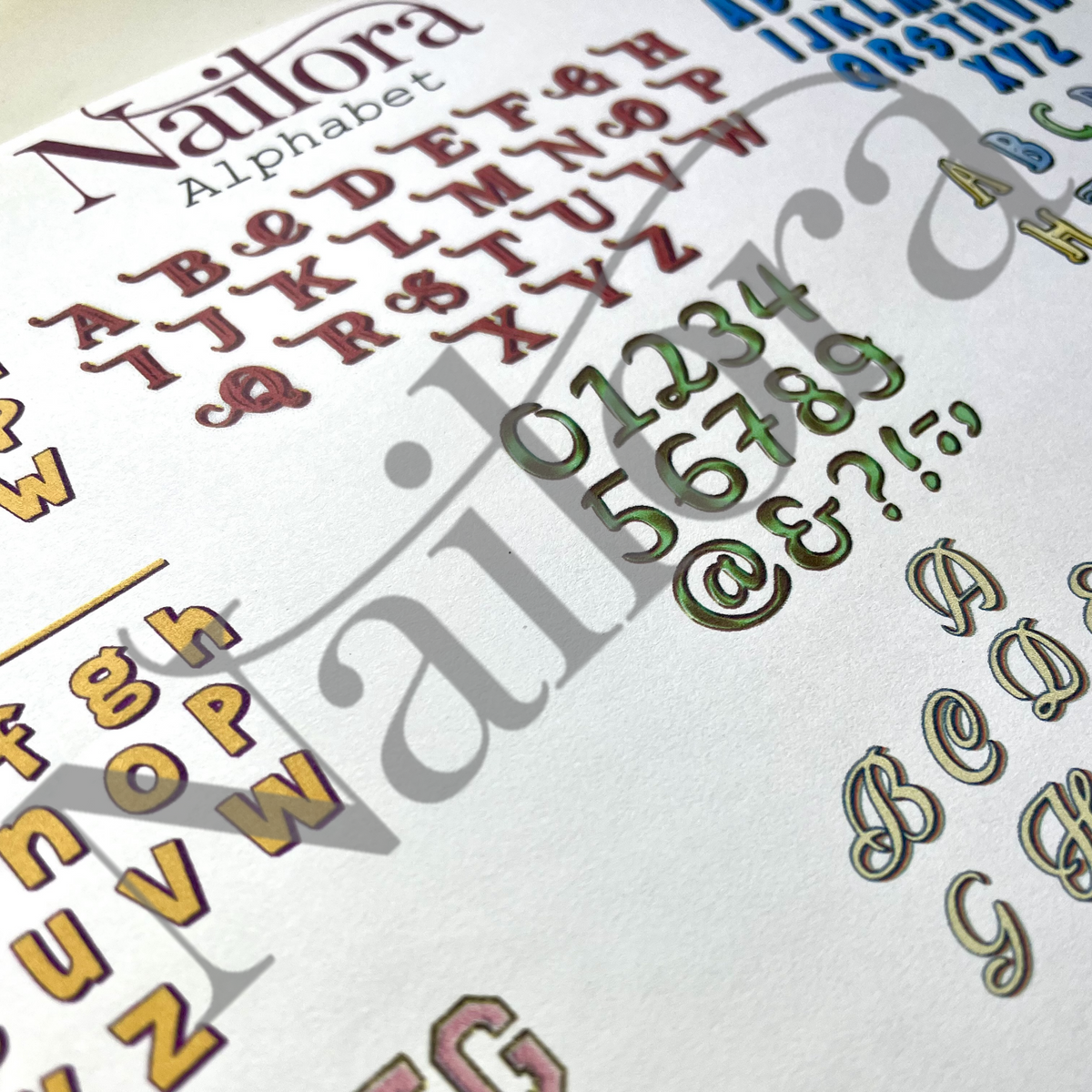 A close-up of a Nailora alphabet nail art stamping plate or decal sheet, showing raised decorative letters and numbers in metallic rose gold, olive green, and gold tones on a white background.