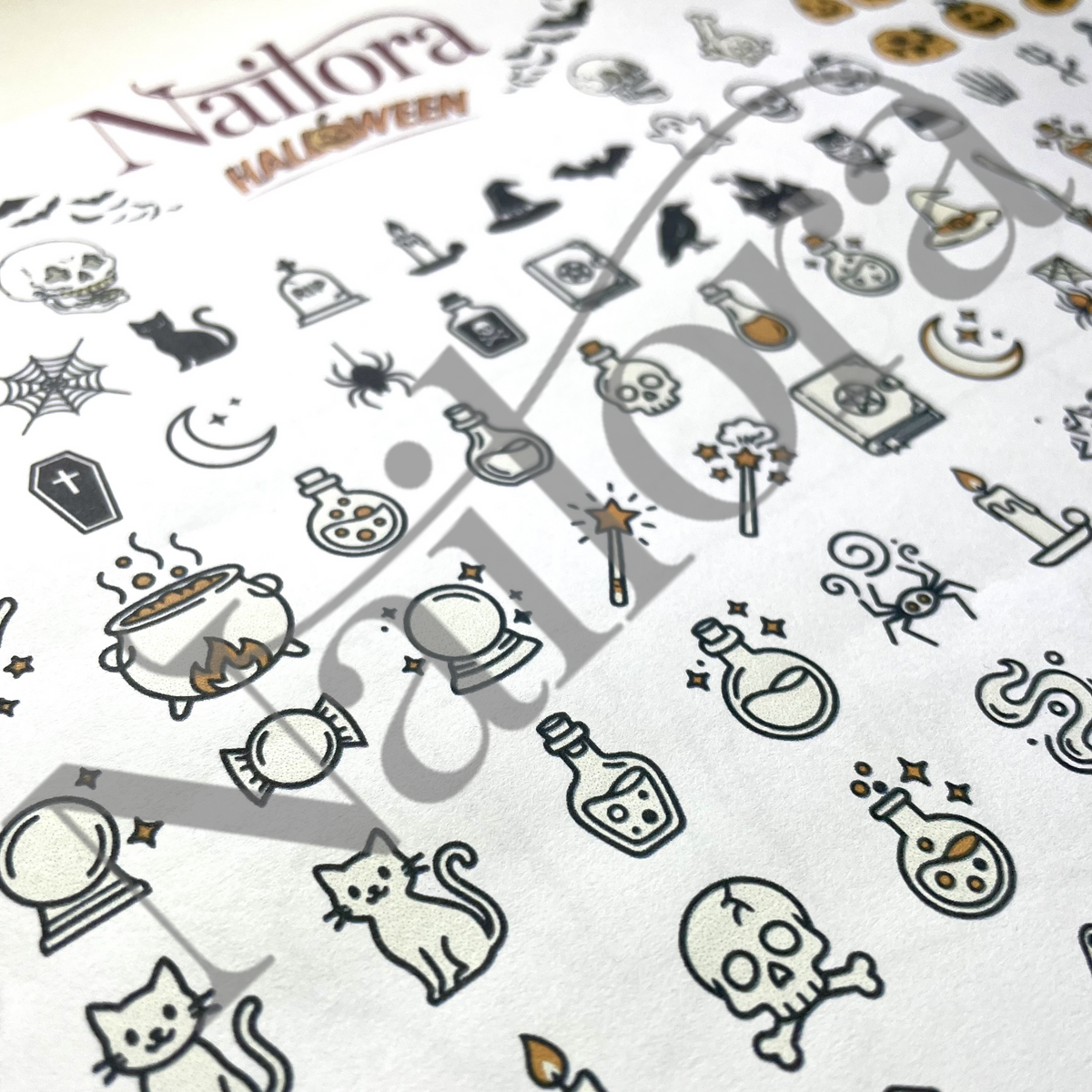 A close-up of a white nail art sheet featuring Halloween-themed illustrations, including skulls, cauldrons, bats, spiders, and candles, with the brand name Nailora and the collection name HALLOWEEN printed at the top.