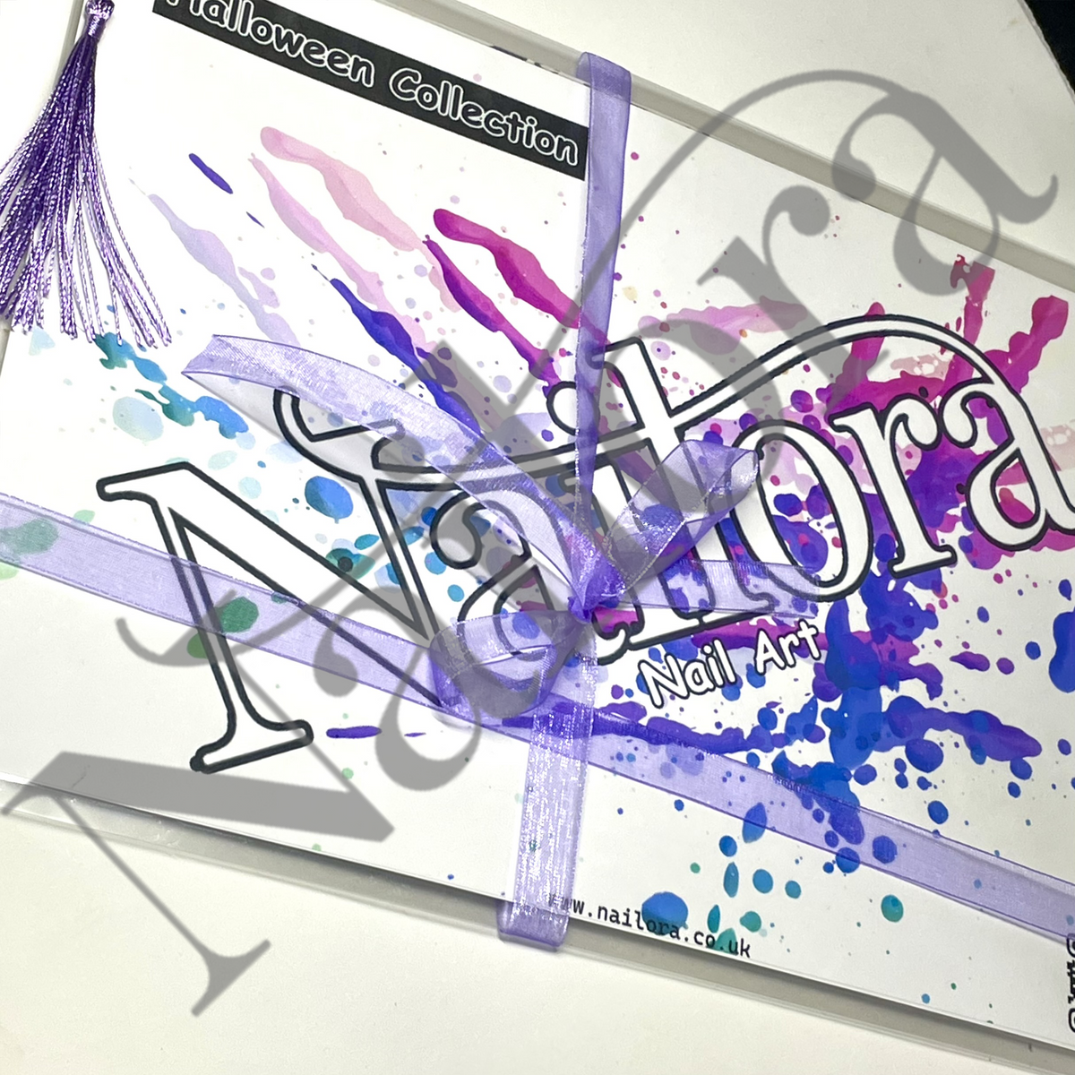 A packaged nail art kit or collection box wrapped with a purple ribbon and tassel, featuring colorful paint splatters in purple, blue, pink, and teal on a white background. Visible text includes 'Halloween Collection' and 'Nail Art', with a large translucent watermark across the image. watermark Nailora