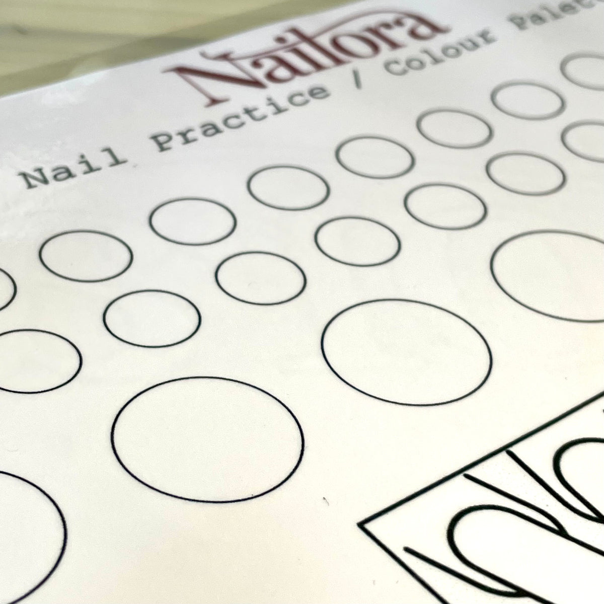 Close-up of a Nailora nail practice color palette sheet showing rows of circular areas and  nail tips in different sizes on white paper.