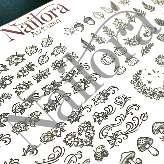A close-up of a nail art sheet labeled 'Nailora Autumn,' showing autumn-themed motifs including leaves, acorns, pumpkins, ferns, flowers, and mushrooms in dark gray on a white surface. Create your own nail stickers