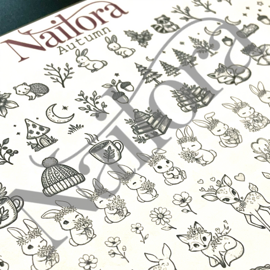 A close-up of a nail art  sheet featuring autumn-themed line art designs, including rabbits, deer, mushrooms, acorns, a mug, and trees. The brand name 'Nailora' is visible at the top left, with 'Autumn' written below it.