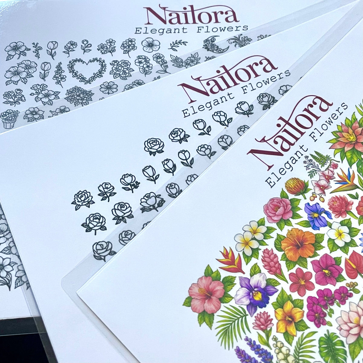 Three sheets of Nailora Elegant Flowers DIY nail art sheets are fanned out, showing different floral designs: black line art on white, and a vibrant multicolor floral pattern on the bottom sheet.