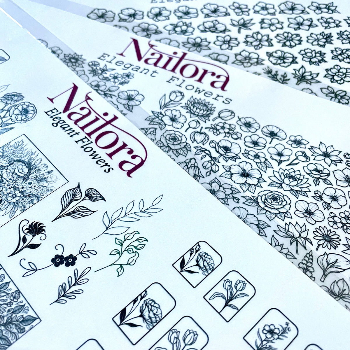 Three sheets of Nailora Elegant Flowers DIY nail art  sheets arranged diagonally, showing black line art floral and botanical designs on white backing sheets.Create your own nail stickers
